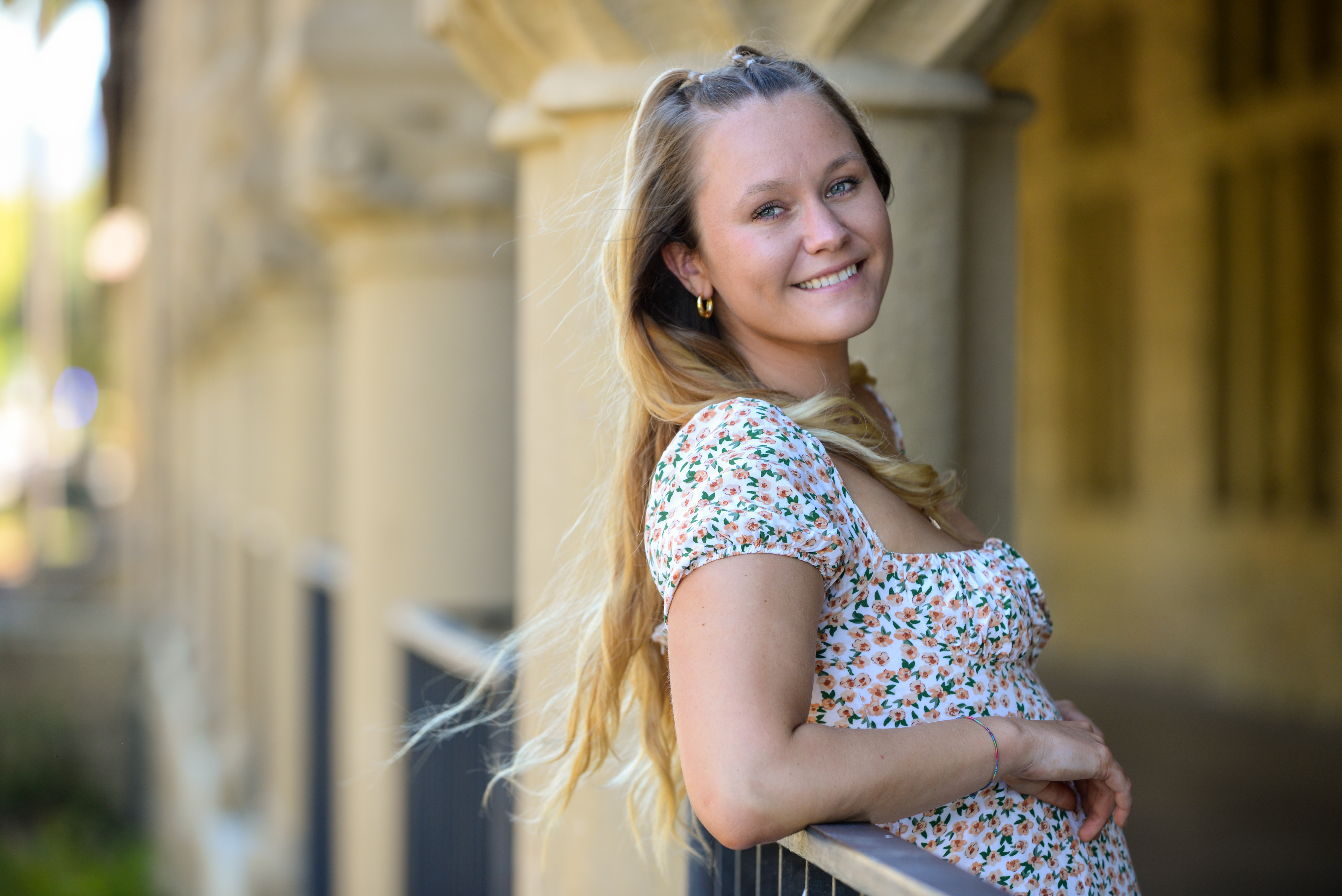 Photo of Lucy Caffrey-Maffei leaning against a railing with a Stanford sandstone colonnade in the background