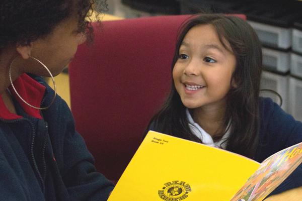 Photo of woman tutoring a young girl in reading