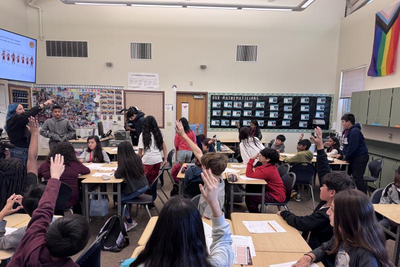 Students raising their hands in a classroom.