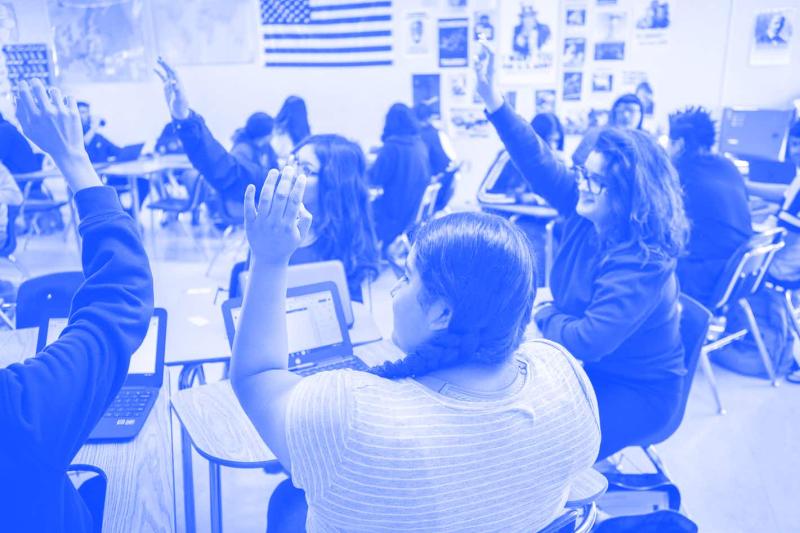 blue tinted photo of a classroom of people raising their hands
