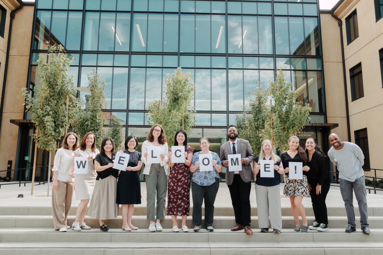Picture of Academic Affairs team holding welcome sign at the steps of the Raikes building.
