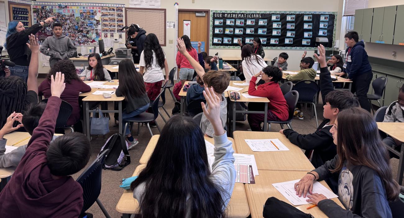 Students raising their hands in a classroom.
