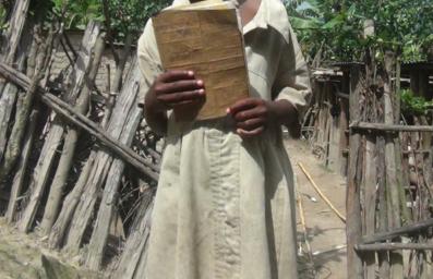 Flora holds the only book she could find in her home. She uses the same book for Kinyarwanda, Maths and English.