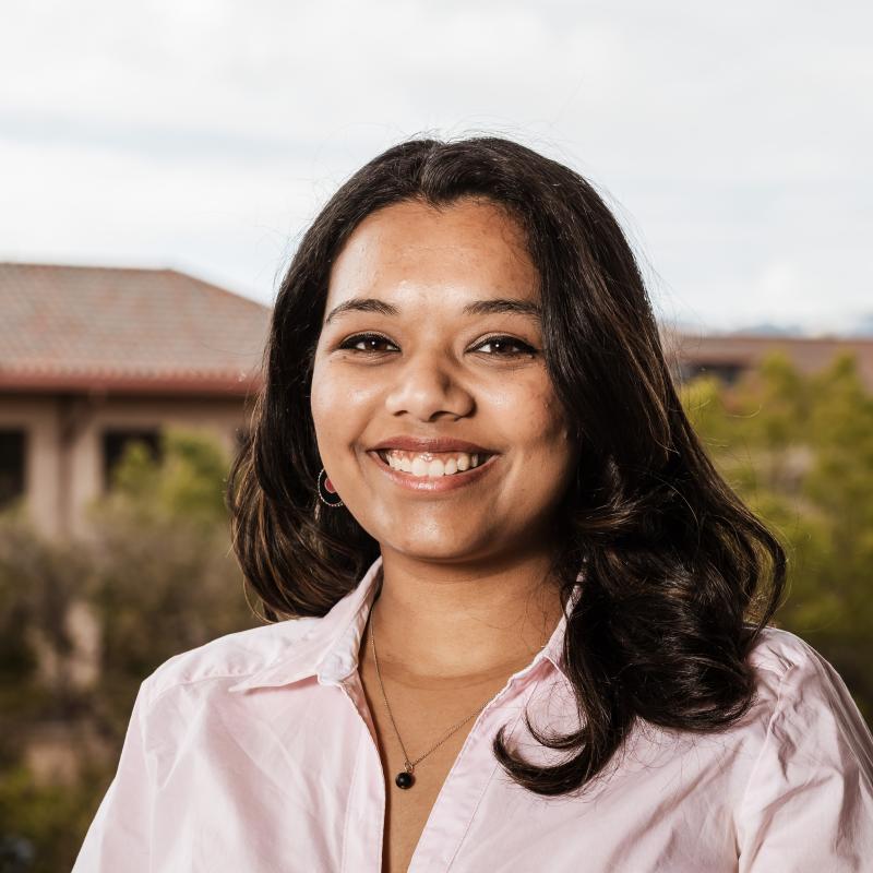 A photograph of Khushi Malde, smiling, with a backdrop of Stanford buildings