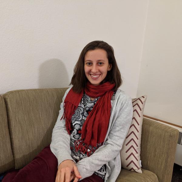 Photo of Ana Trindade Ribeiro sitting on a couch, smiling